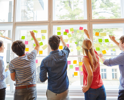 Eine Gruppe junger Menschen steht vor einem Fenster und befestigt Post Its darab