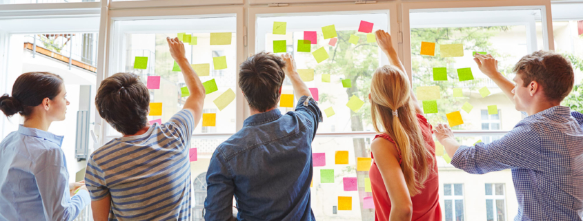 Eine Gruppe junger Menschen steht vor einem Fenster und befestigt Post Its darab
